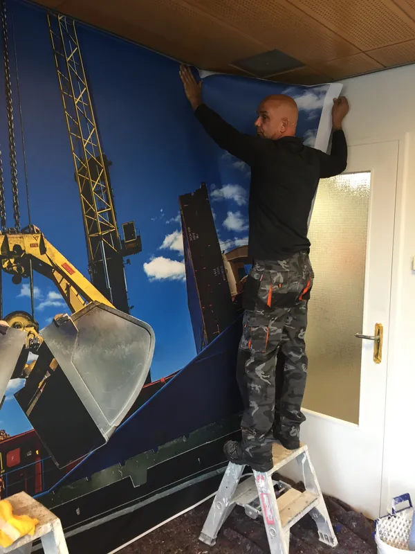Behanger op een trapje brengt een baan fotobehang aan op een kantoorwand